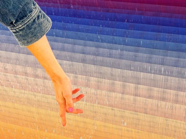 A visitor reaching toward a thread installation in sunset colors