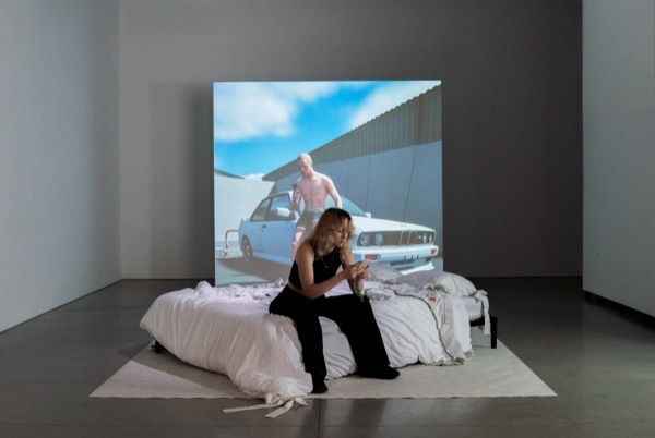 A wider view of the installation: the bed, the long white sheets and the screen