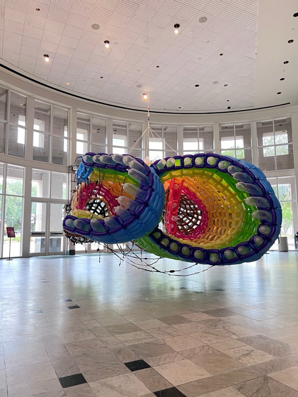 A rainbow-colored sculpture suspended in a round room with tall windows