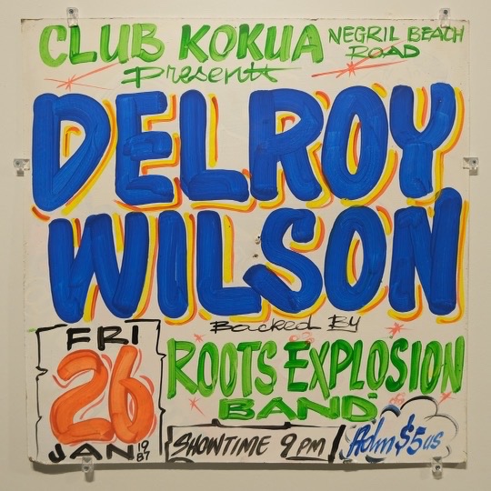 A sign for Delroy Wilson with Roots Explosion Band at Club Kokua, in red, blue and yellow