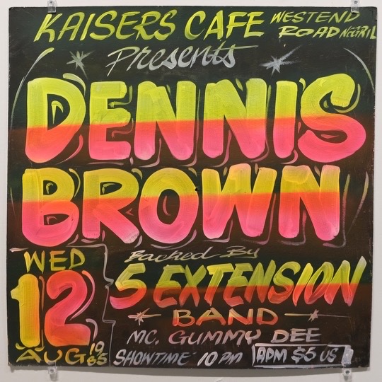 A Dennis Brown sign in pink and yellow on black