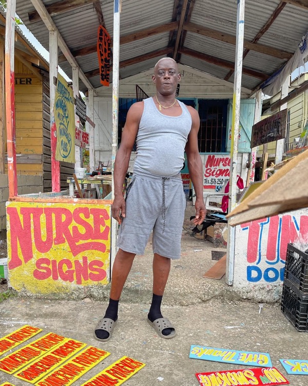 Nurse standing outside his sign shop, surrounded by painted signs