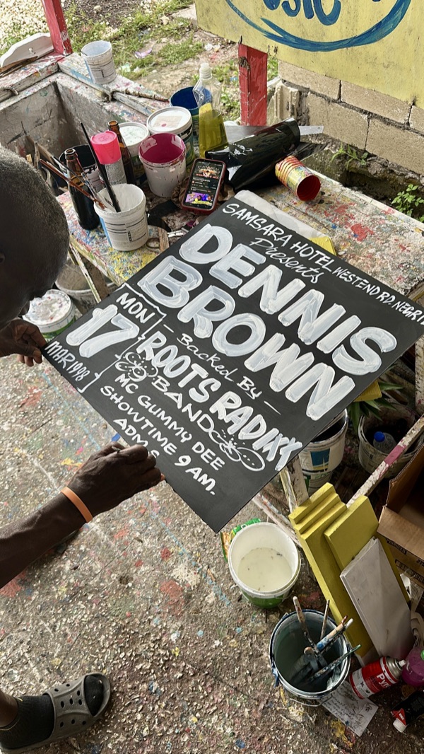 A Dennis Brown sign in progress on a paint-spattered workbench