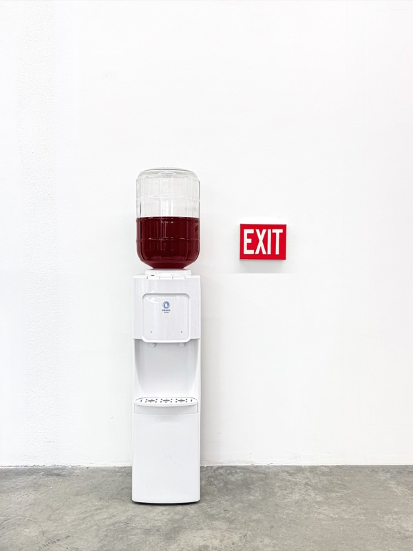 An office water cooler filled with red liquid, next to a red exit sign
