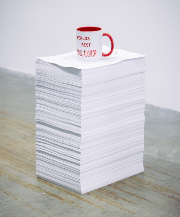 A tall stack of paper topped with a WBS coffee mug