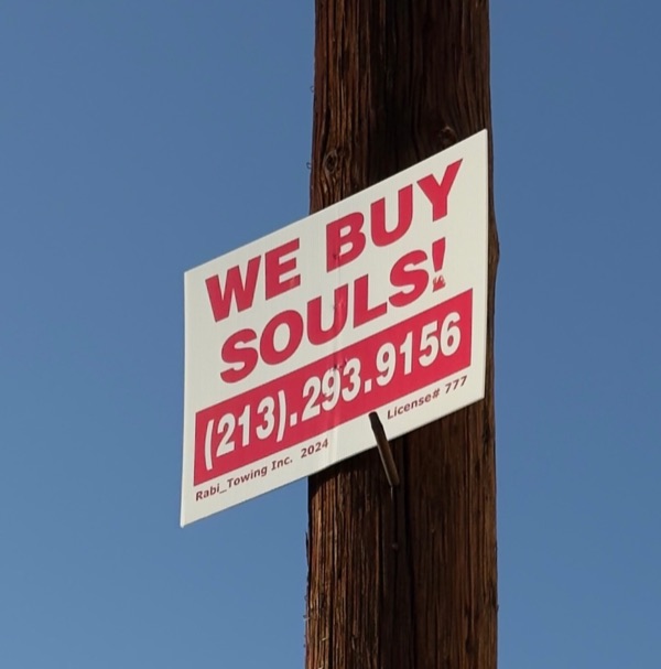A red and white WE BUY SOULS! sign with a phone number, on a wooden pole