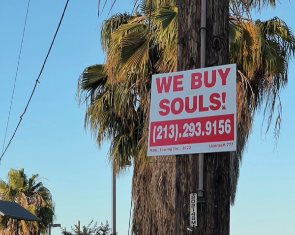 A WE BUY SOULS! sign on a pole in front of palm trees