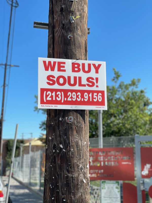 A WE BUY SOULS! sign on a pole against a blue sky