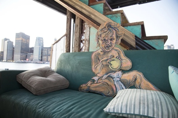 Inside the sculpture, a painted figure sits among cushions with the city skyline beyond