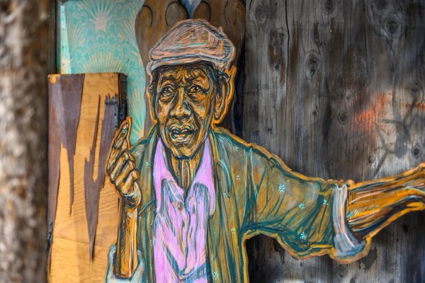 A painted portrait of an older man in a cap and a patterned jacket