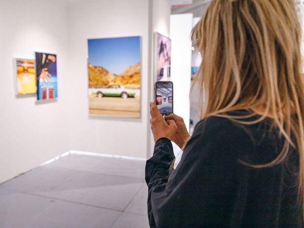 A visitor photographs a painting in a gallery booth