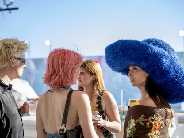 Friends in bold hats talking in the sun, one in a large blue hat