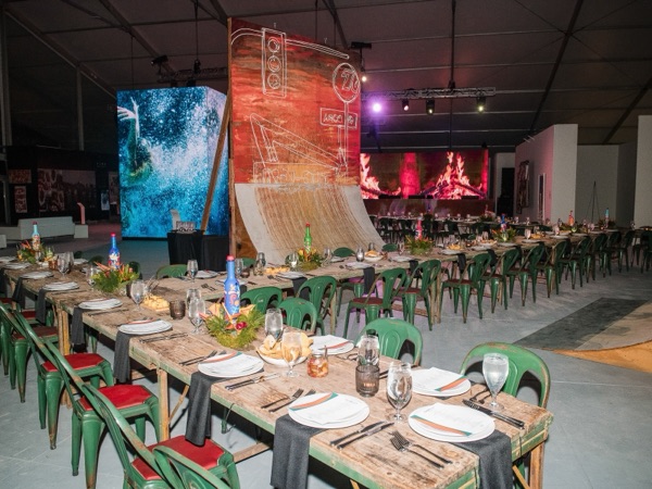 Long dinner tables set with green chairs, beneath large glowing artworks