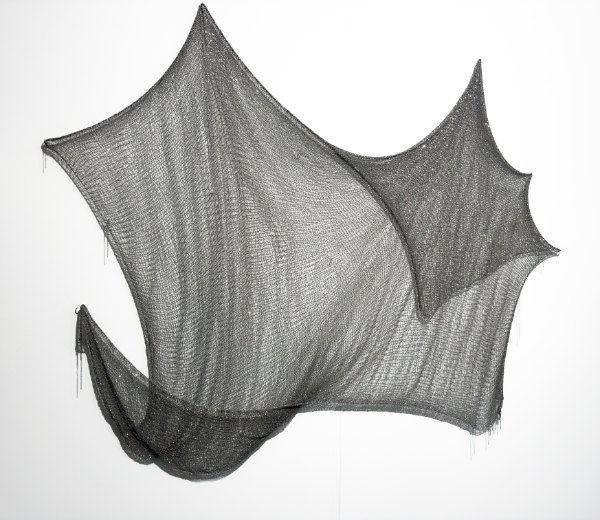 Safety Net by Natalia Fedner: a dark woven metal mesh sculpture stretched into angular, wing-like points against a white wall