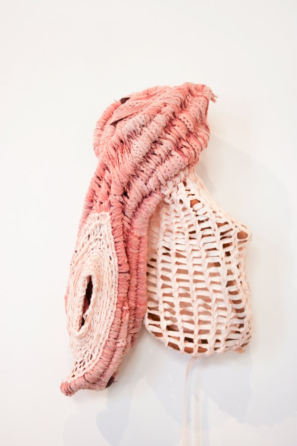 Basket Body by Yusuf Dubois Abdul Lateef: a coiled wall sculpture in coral pink and pale peach, one side tightly wrapped, the other an open lattice like basketry