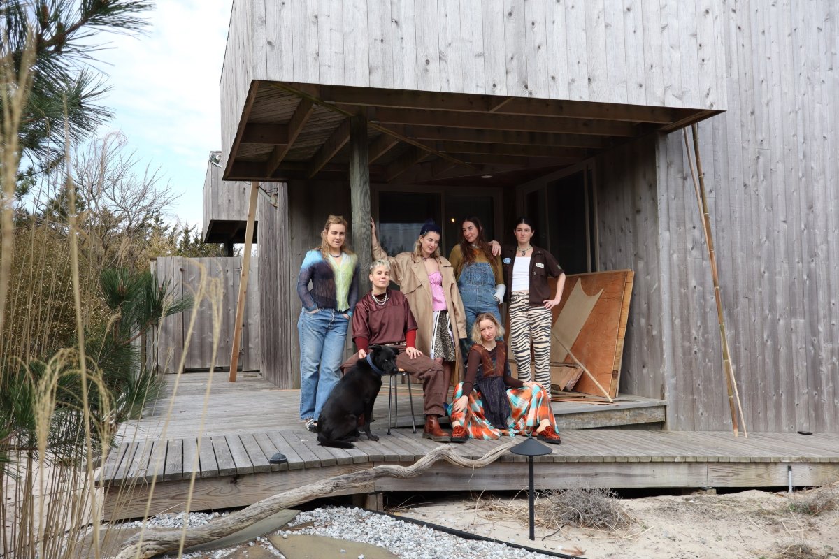 The Bamboo House artists with a black dog on the deck of a weathered wood house, dune grass in the foreground