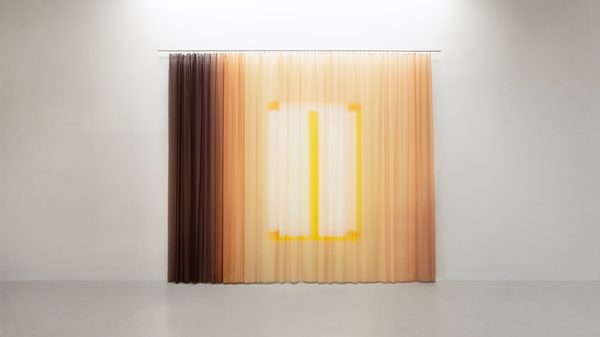 Imprint Yellow Dusk by Yvonne Mak: a curtain hung on a white wall, faded from deep brown at the left edge to pale yellow, with a brighter yellow rectangle at its centre