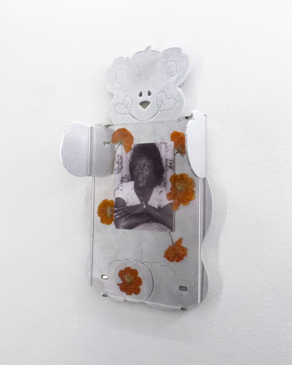 Teddy Bear Frames by Sam Dybeck: a cut-metal teddy bear frame holding a black-and-white photograph of a person, decorated with pressed orange flowers, on a white wall