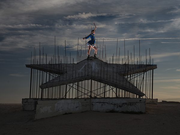 Mad Star 2 by Richeille Formento: a majorette in a blue uniform raises a baton on top of a large concrete star bristling with rebar, in open desert at dusk